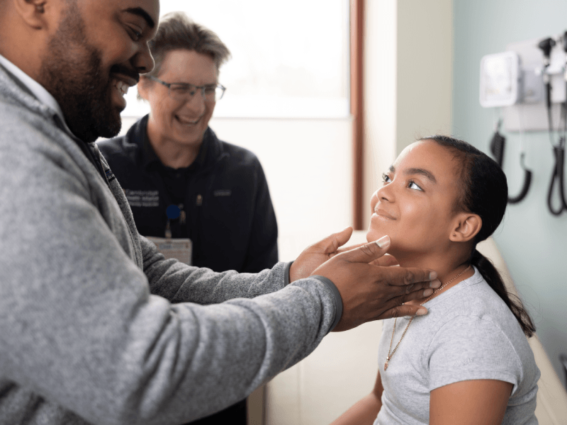 Two CHA doctors providing care to a teenage girl in a brightly lit exam room
