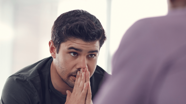 Young man with dark hair with hands folded in front of his face