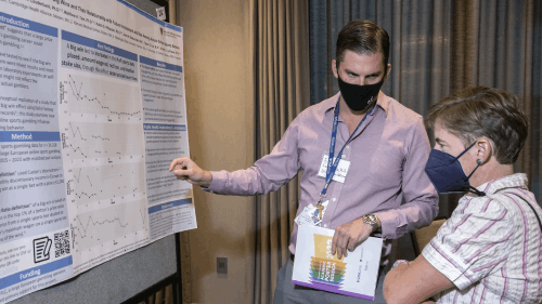 Academic poster session, presenter is explaining details from the poster to a woman