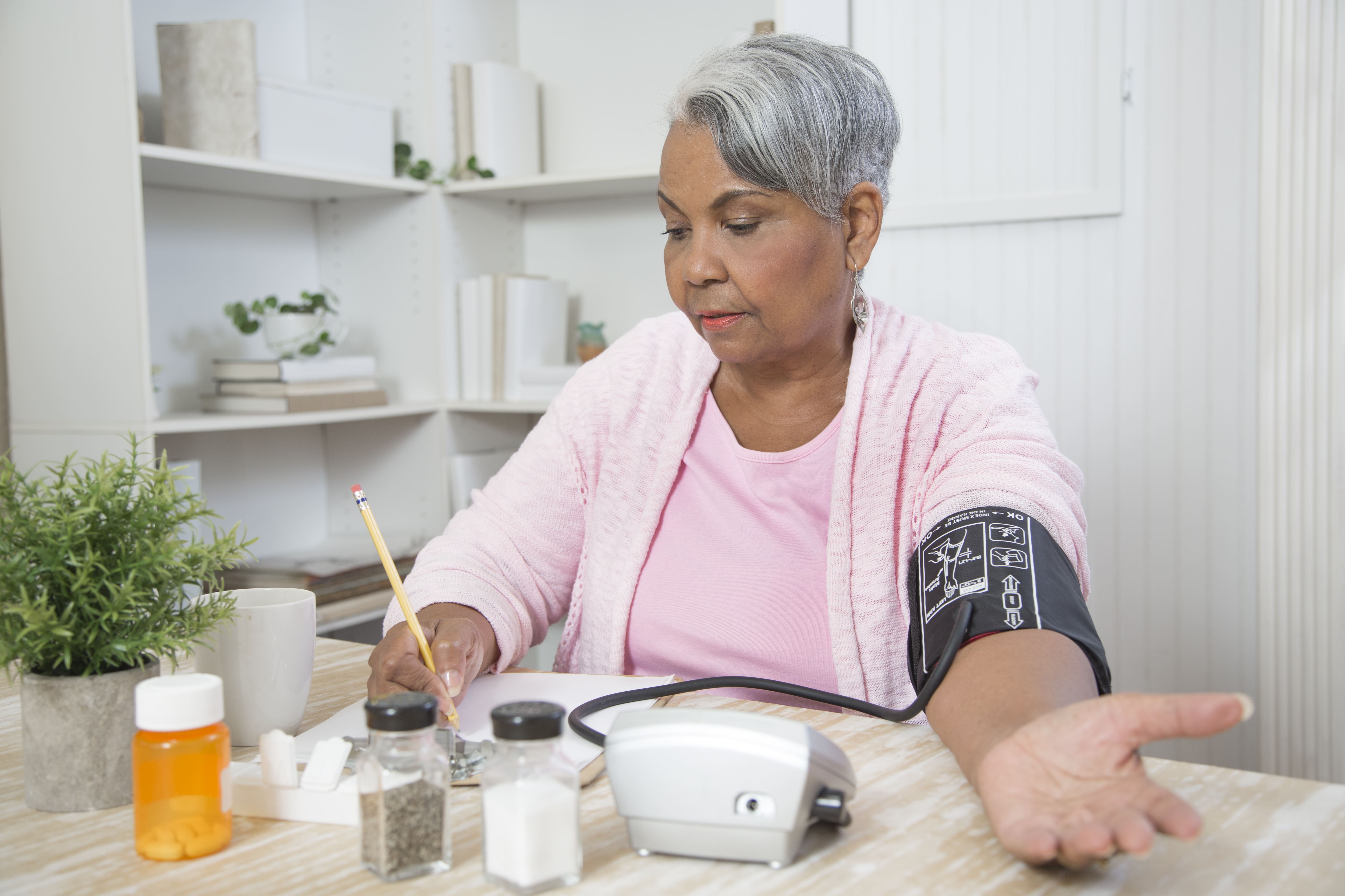 Black woman taking her blood pressure at home, sitting at a kitchen table