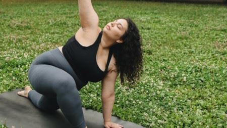 p[hoto of a white woman doing yoga and stretching with her arm raised. 